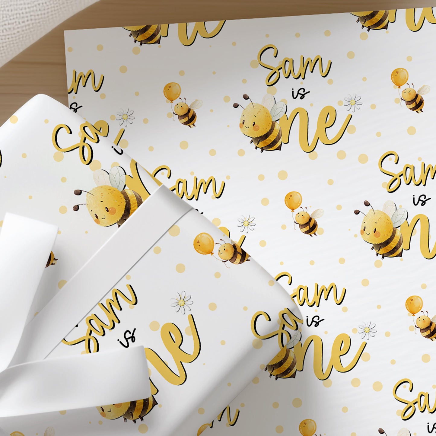 a white gift box with a repeating pattern of yellow bees and the text "Sam is one" printed on it.