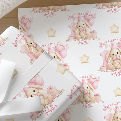 Close-up of personalised first birthday wrapping paper featuring a cute bunny rabbit, pink number one, balloons and presents on premium white wrapping paper.