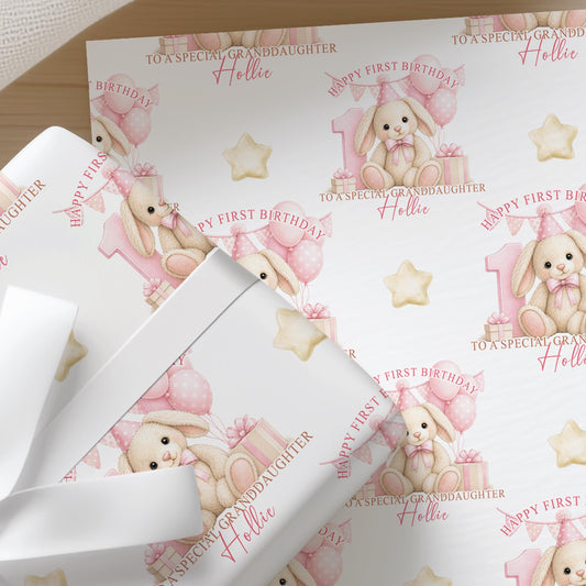 Close-up of personalised first birthday wrapping paper featuring a cute bunny rabbit, pink number one, balloons and presents on premium white wrapping paper.
