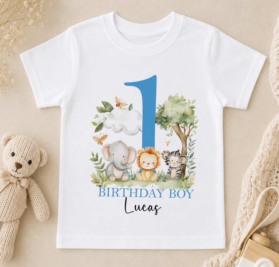 A white t-shirt with a blue number one and illustrations of various animals, including an elephant, lion, and tiger, along with the text "BIRTHDAY BOY Lucas".