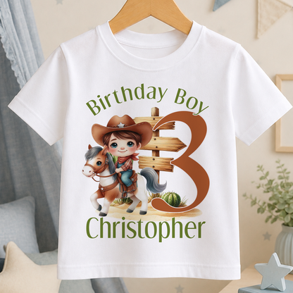 A white t-shirt with a cartoon image of a boy riding a horse and a wooden sign, along with the text "Birthday Boy Christopher" printed on it.