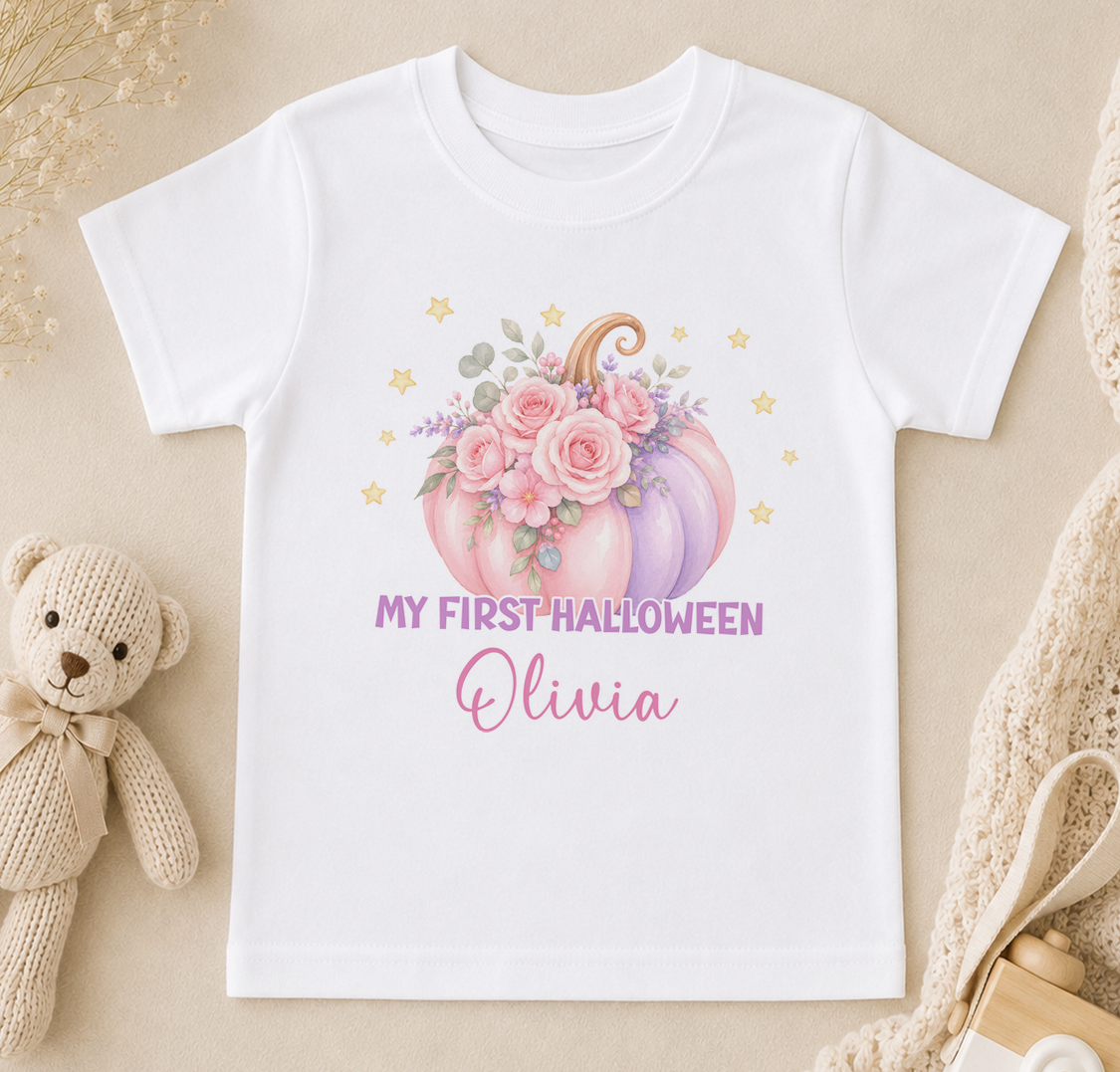 A white t-shirt with a graphic design featuring a pumpkin with flowers and stars, along with the text "My first Halloween Olivia" printed on it.