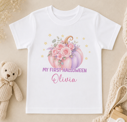A white t-shirt with a graphic design featuring a pumpkin with flowers and stars, along with the text "My first Halloween Olivia" printed on it.