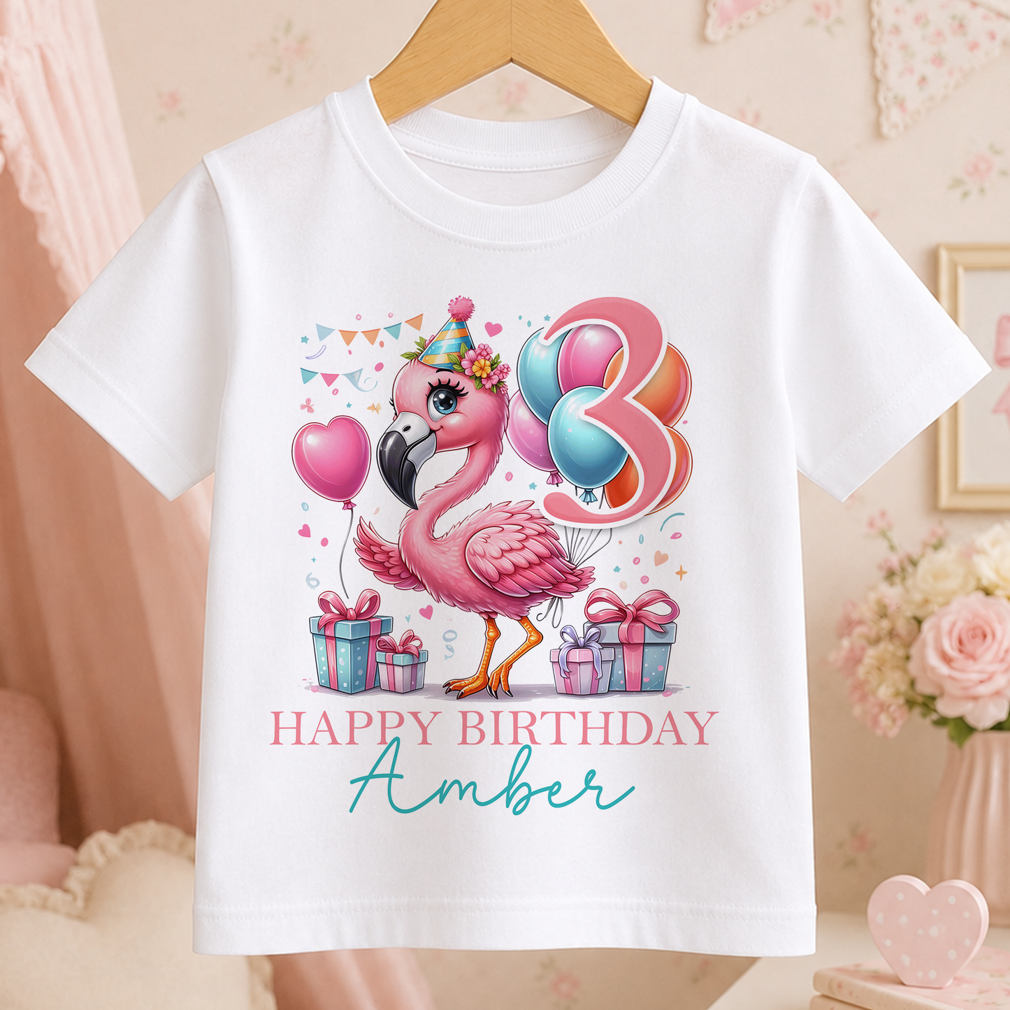 A white t-shirt with a pink flamingo and birthday decorations, including balloons and presents, along with the text "Happy Birthday Amber".