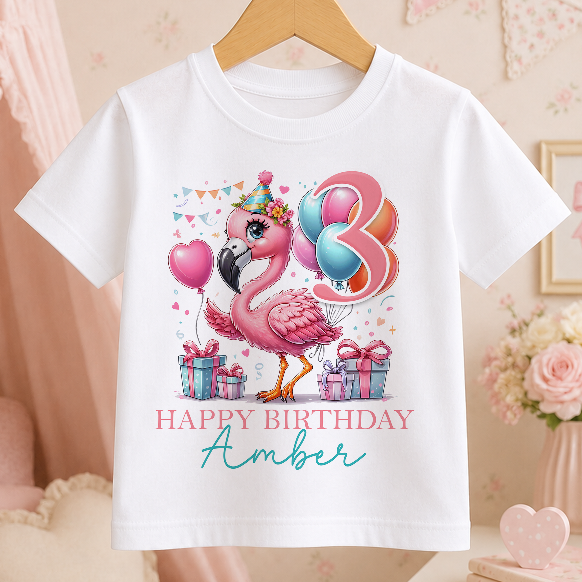 A white t-shirt with a pink flamingo and birthday decorations, including balloons and presents, along with the text "Happy Birthday Amber".