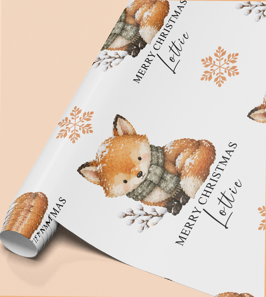 a roll of wrapping paper with a festive design of a fox wearing a scarf and surrounded by snowflakes. The text "Merry Christmas Lottie" is written on the paper, indicating a personalized gift for someone named Lottie.