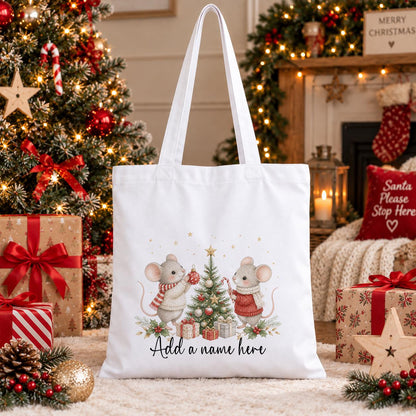 White cotton tote bag printed with two watercolour mice in jumpers decorating a Christmas tree, above a name in script.