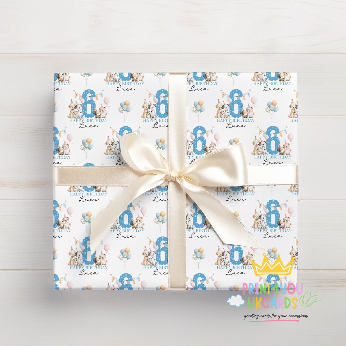 Top-down view of a gift wrapped in personalised dog birthday wrapping paper tied with a cream ribbon bow, printed with party dogs, balloons and a blue number 6 with the name Luca