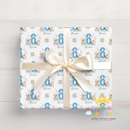 Top-down view of a gift wrapped in personalised dog birthday wrapping paper tied with a cream ribbon bow, printed with party dogs, balloons and a blue number 6 with the name Luca