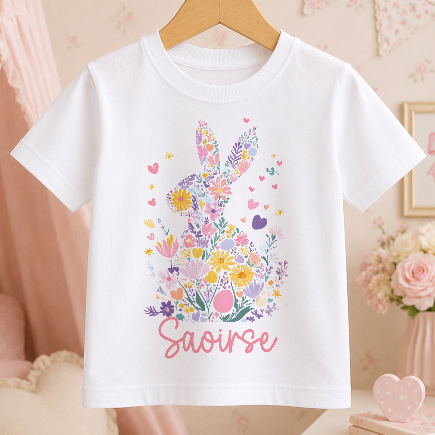 A white t-shirt with a colorful floral design and the name "Saoirse" printed on it, hanging on a wooden hanger.