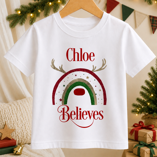 A white t-shirt with a Christmas-themed design, including a rainbow and the text " Chloe Believes".