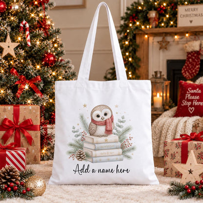 Personalised Christmas tote bag in white cotton with a cream owl in a pink scarf on a stack of books, pine and berries, with a name beneath