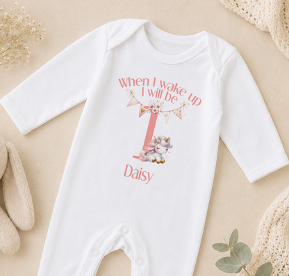 A white onesie with a personalized text and a unicorn graphic, likely for a baby's first birthday.