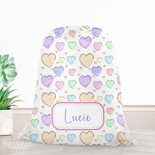Drawstring PE bag printed with a hand-drawn rainbow heart design in pastel shades, personalised with a child's name across the front