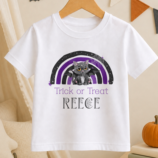 A white t-shirt with a graphic design featuring a cat and a rainbow. The cat is depicted with a bat-like appearance, and the rainbow has purple and black colors. The text on the t-shirt says "Trick or Treat REECE".