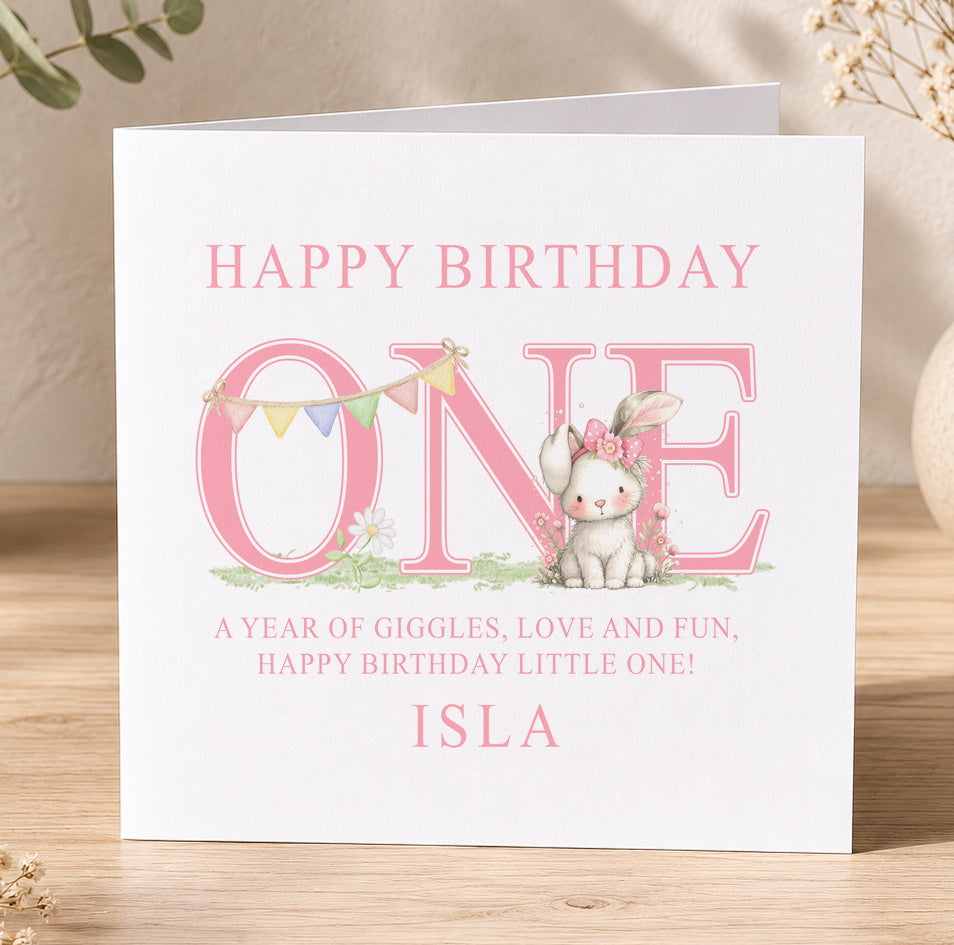 Pink first birthday card featuring a floppy-eared bunny and colourful bunting, printed with the name Isla and age one as a personalisation example.