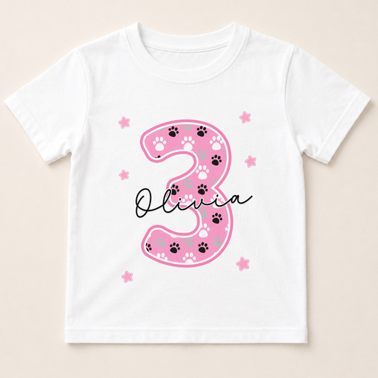 A white t-shirt with a pink number 3 and paw prints design, along with the name "Olivia" written below it.
