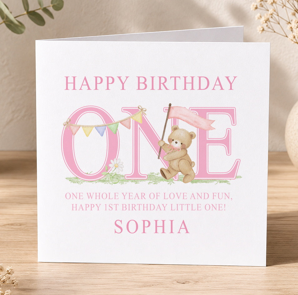 Personalised first birthday card for a baby girl featuring a teddy bear holding a pink 'Happy Birthday One' banner, shown personalised with the name Sophia