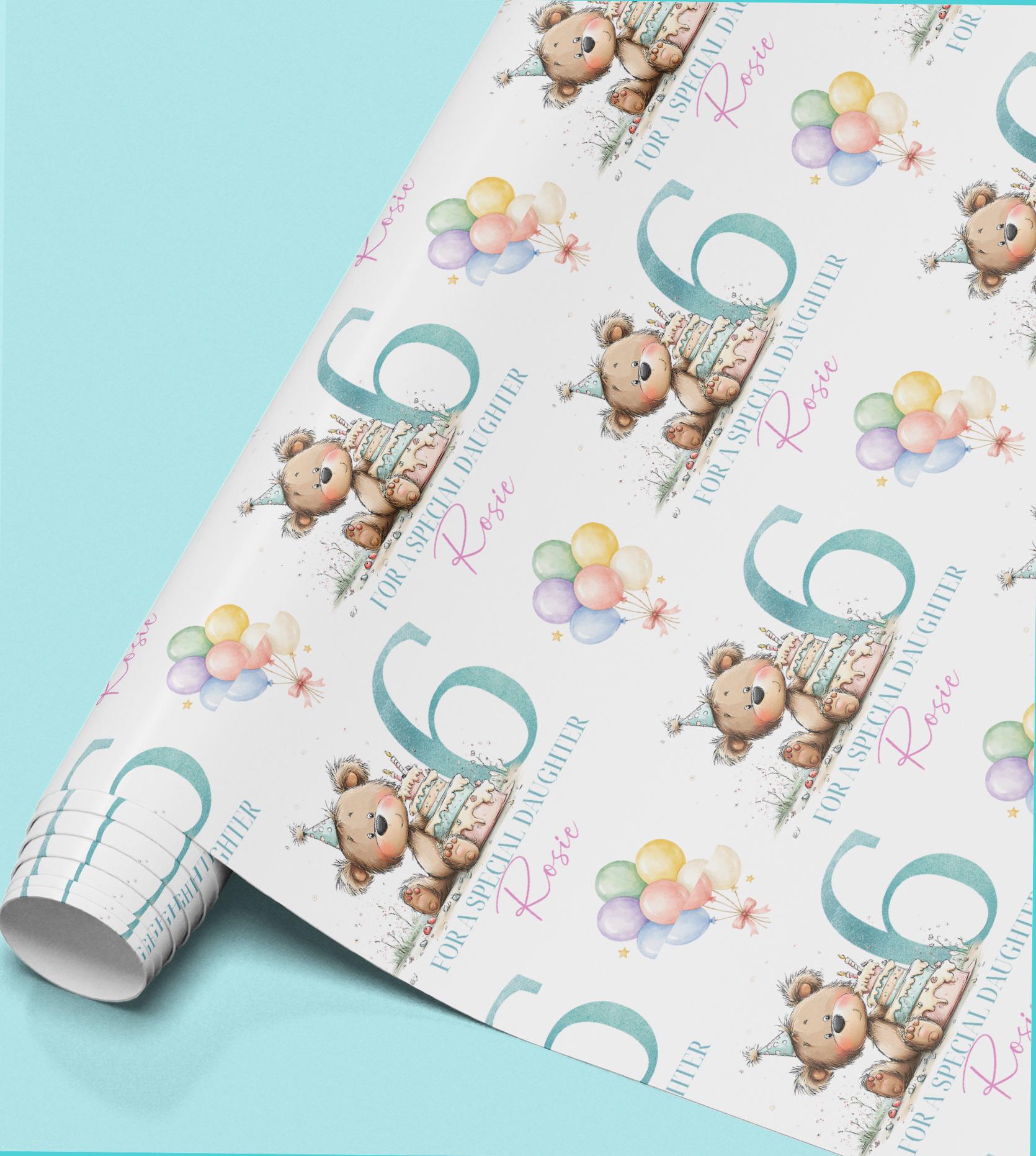 a roll of wrapping paper with a repeating pattern of a teddy bear wearing a party hat and holding a birthday cake, along with colorful balloons.