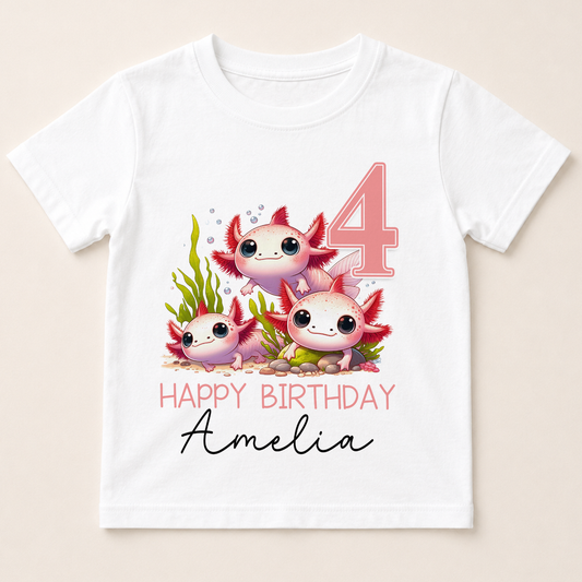 A white t-shirt with a graphic design featuring three cartoon axolotls, which are aquatic salamanders, along with the text "Happy Birthday Amelia" and the number "4".