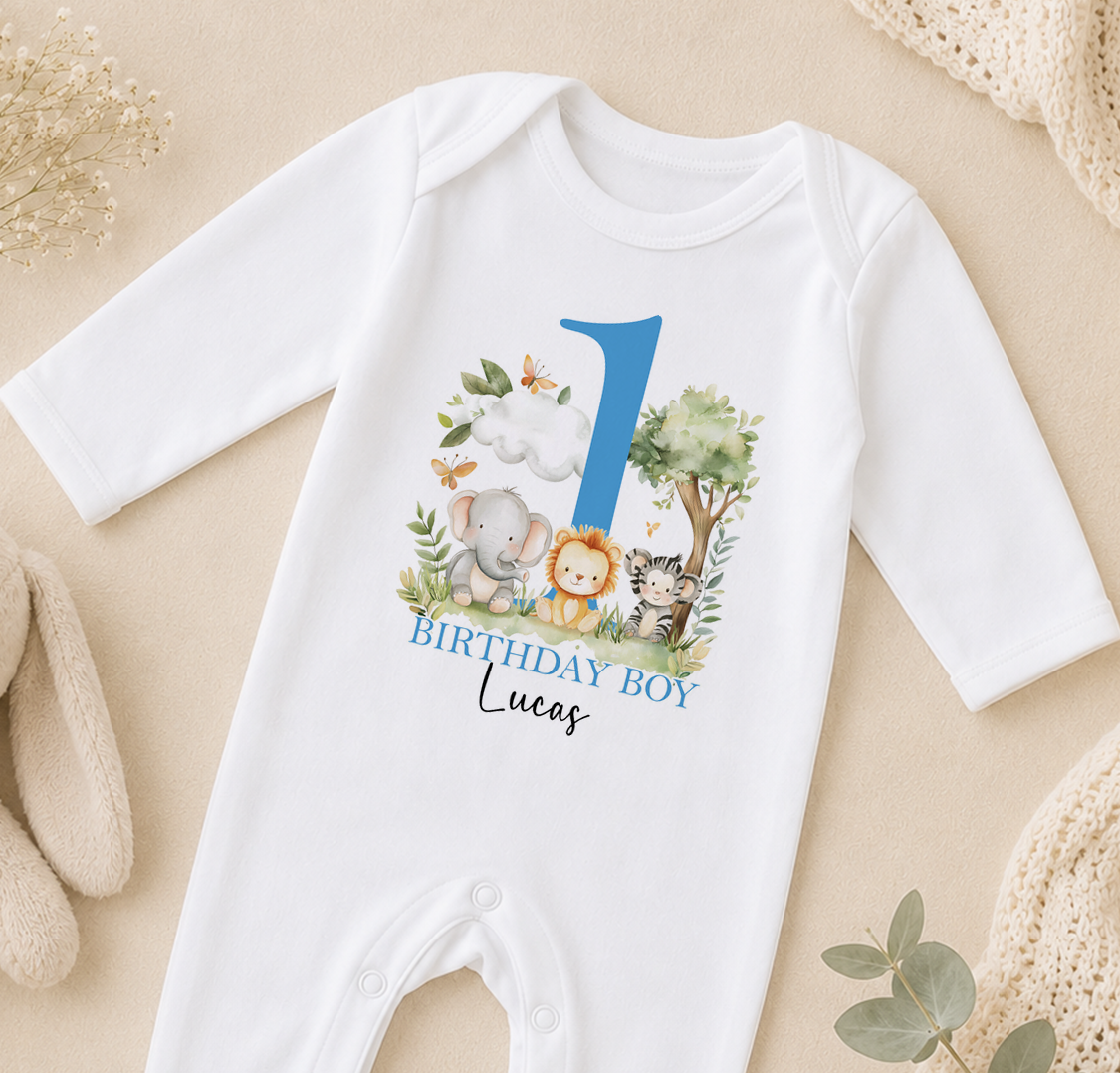A white onesie with a blue number 1 and various animal illustrations, including an elephant, lion, and tiger, along with the text "BIRTHDAY BOY Lucas".