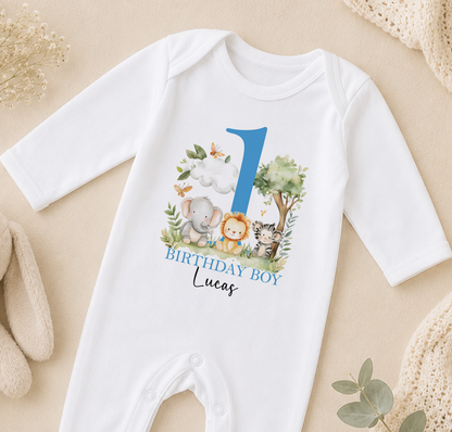 A white onesie with a blue number 1 and various animal illustrations, including an elephant, lion, and tiger, along with the text "BIRTHDAY BOY Lucas".