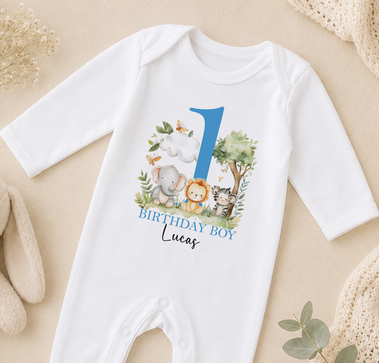 A white onesie with a blue number 1 and various animal illustrations, including an elephant, lion, and tiger, along with the text "BIRTHDAY BOY Lucas".