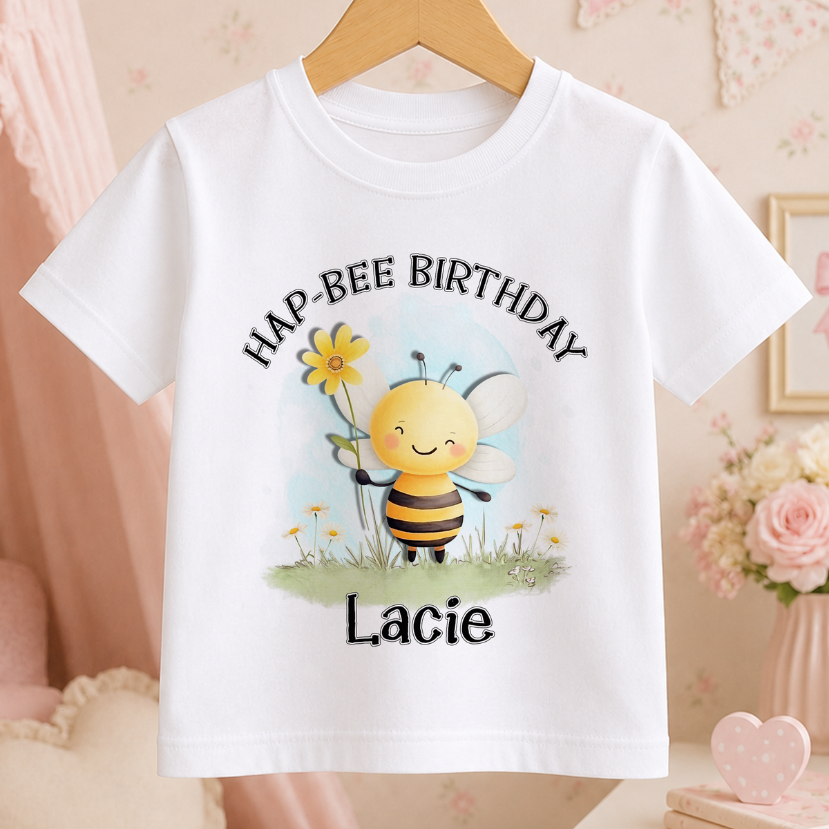 A white t-shirt with a cartoon bee holding a flower and the text "HAP-BEER BIRTHDAY Lacey" printed on it.