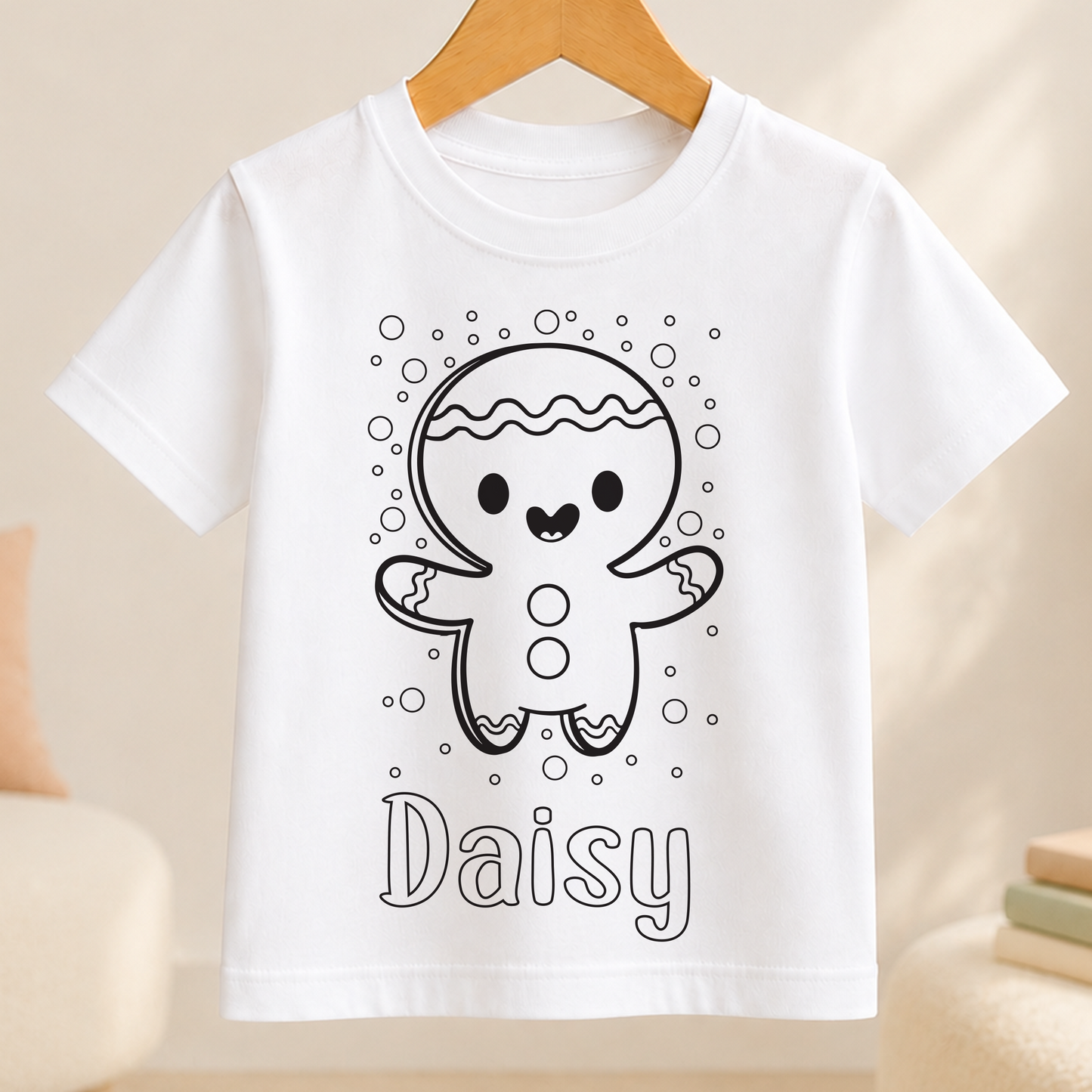 A white t-shirt with a black and white illustration of a smiling gingerbread man surrounded by bubbles. The name "Daisy" is written below the illustration.