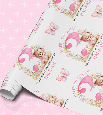 The image is a roll of wrapping paper with a repeating pattern of pink and white images, including teddy bears, butterflies, and flowers. The text on the paper reads "Happy Birthday Hannah" and "To a lovely grandchild Hannah".