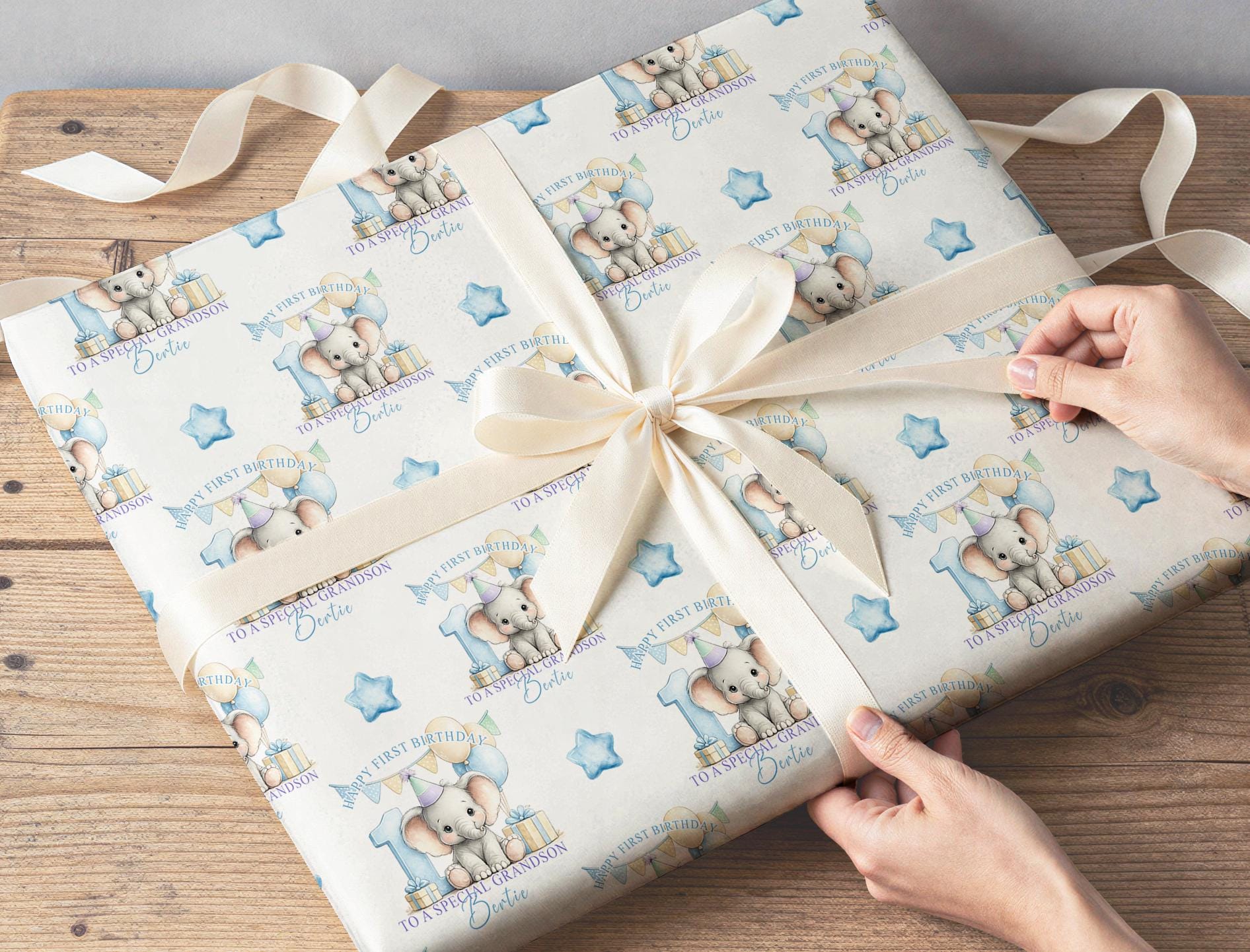 Personalised baby elephant wrapping paper wrapped around a gift with ribbon, featuring the custom name, blue number one and balloons.