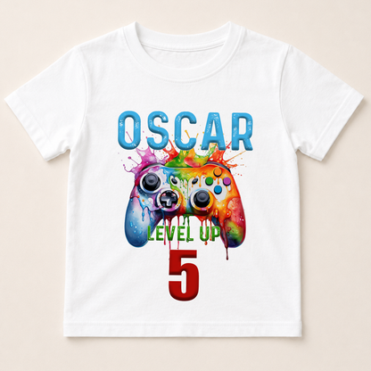 A white t-shirt with a colorful graphic design featuring a video game controller and the text "OSCAR LEVEL UP 5" printed on it.