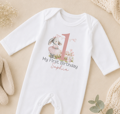 A white onesie with a pink bunny and the text "My first birthday Sophia" printed on it, along with a large number "1" and a banner.