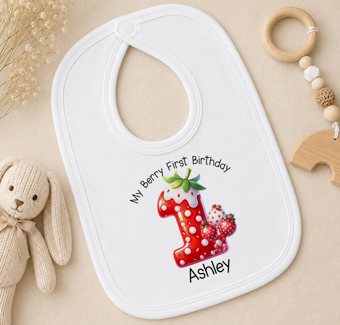 A white bib with a personalized design for a baby's first birthday, featuring a red number one with strawberries and a green leaf.