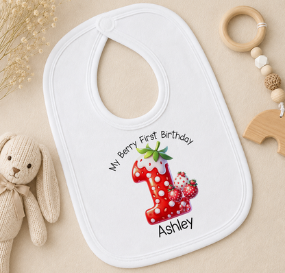 A white bib with a personalized design for a baby's first birthday, featuring a red number one with strawberries and a green leaf.