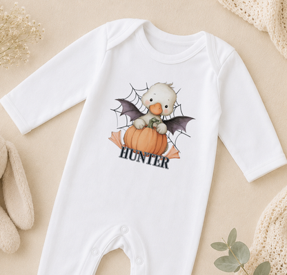 A white onesie with a cartoon image of a baby duck wearing a spider web costume and holding a pumpkin, with the name "Hunter" printed on it.