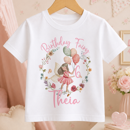 A white t-shirt with a birthday fairy design and the text "Birthday Fairy 6 Theia" printed on it.