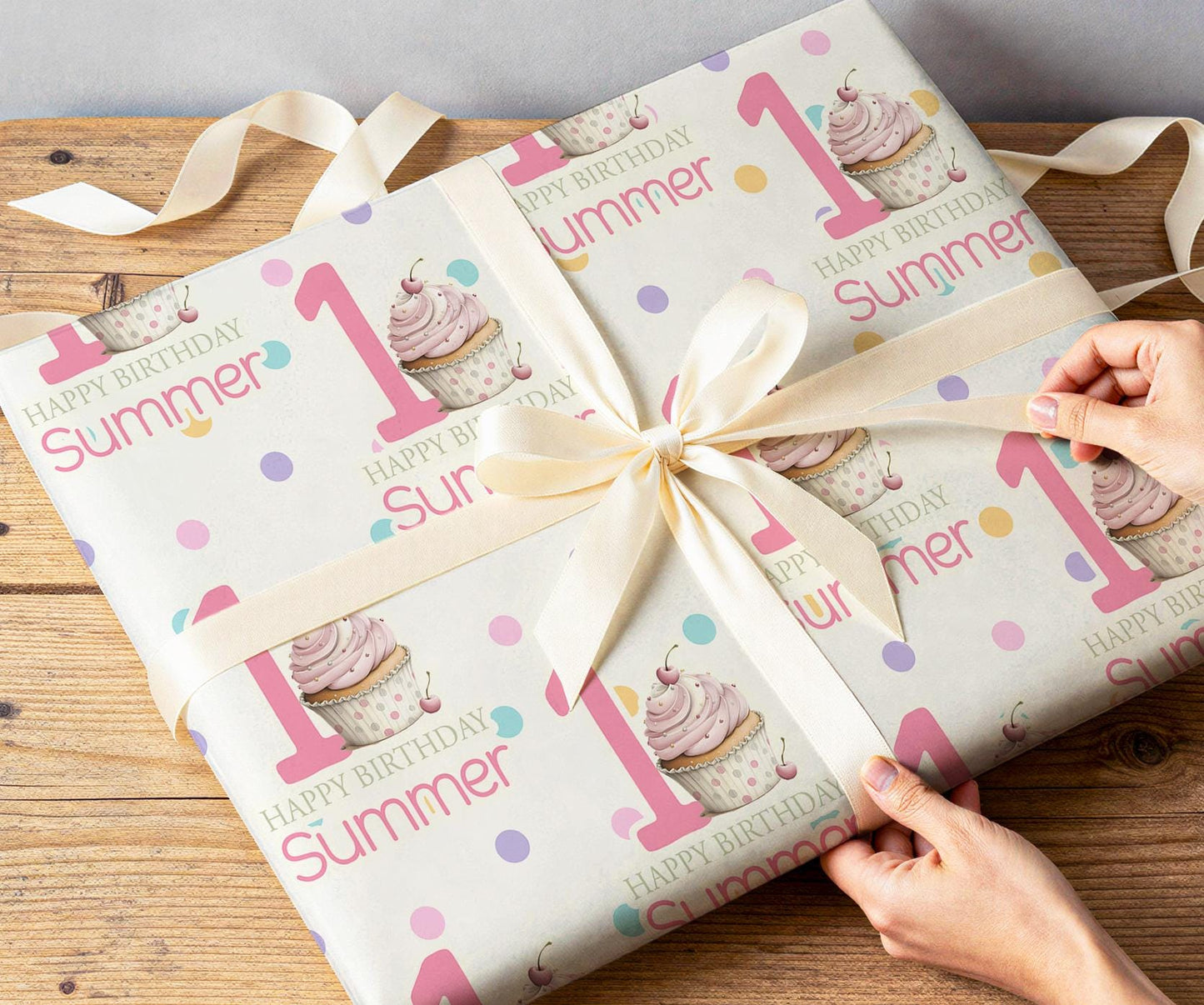 Close-up of hands wrapping a present in the personalised pink cupcake and confetti dot wrapping paper with white ribbon