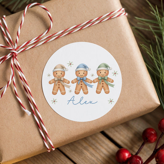 A brown gift box wrapped with a red and white striped ribbon, featuring a round sticker with three smiling gingerbread men wearing hats and scarves.