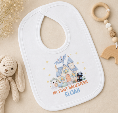 A white baby bib with a Halloween-themed design, featuring a house, a cat, and a bat, along with the text "My first Halloween Elijah".