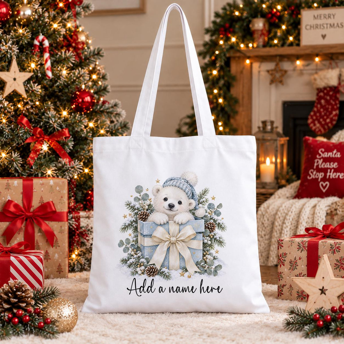 White cotton tote bag printed with a watercolour polar bear cub in a bobble hat peeping from a blue present, above a name.