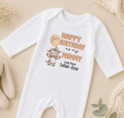 A white onesie with a cartoon cow and text printed on it, placed on a beige surface.