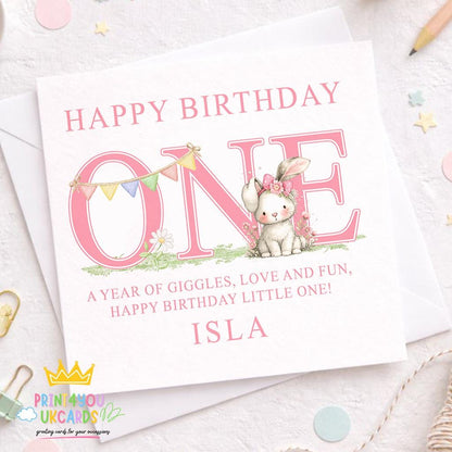 Square first birthday greeting card shown at an angle to display the pink bunny design and card stock.