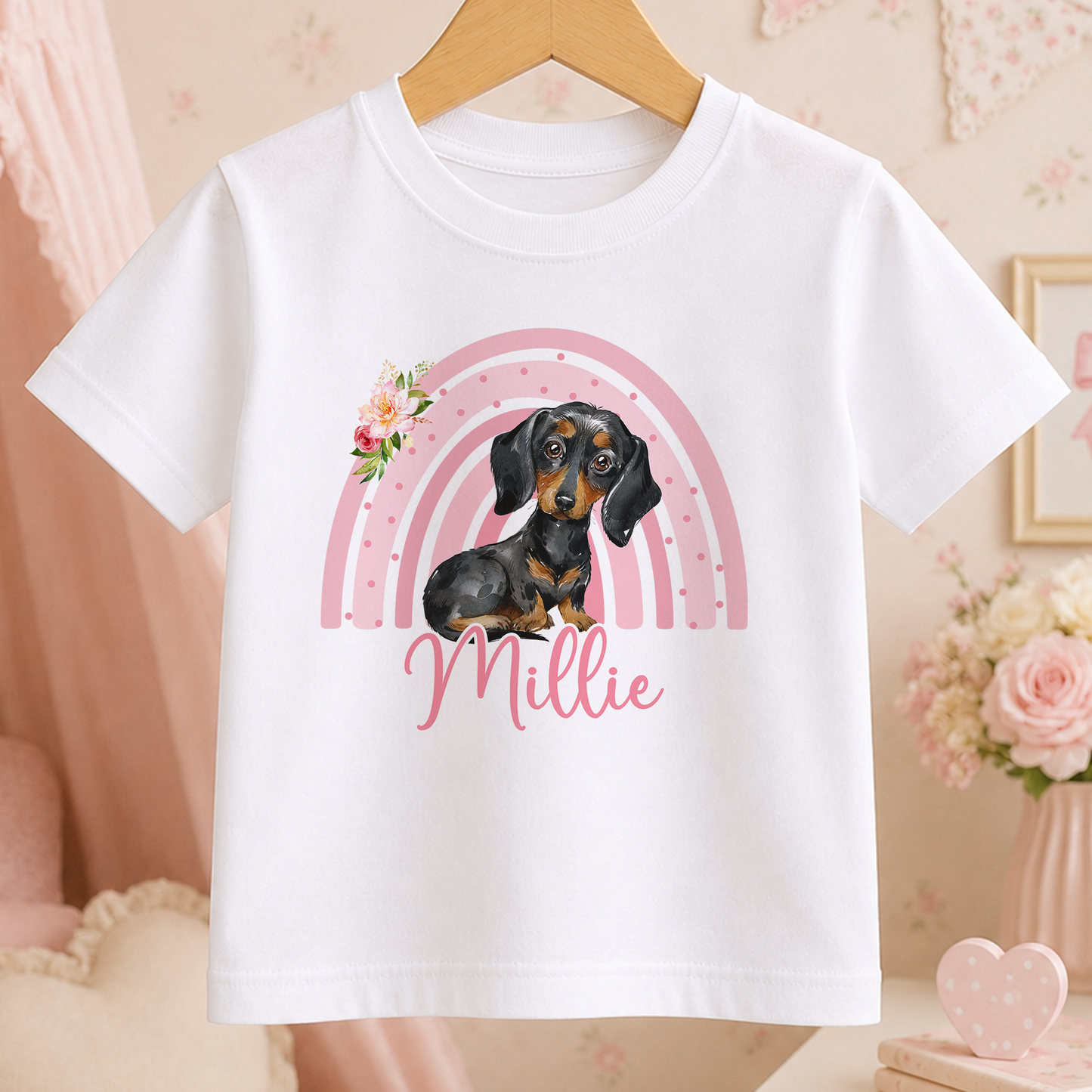A white t-shirt with a printed design of a dachshund dog and a pink rainbow. The name "Millie" is written below the dog.