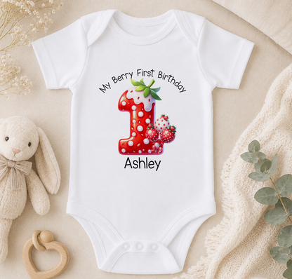 A white onesie with a red number one and strawberries printed on it, along with the text "My Berry First Birthday Ashley" printed on the front.