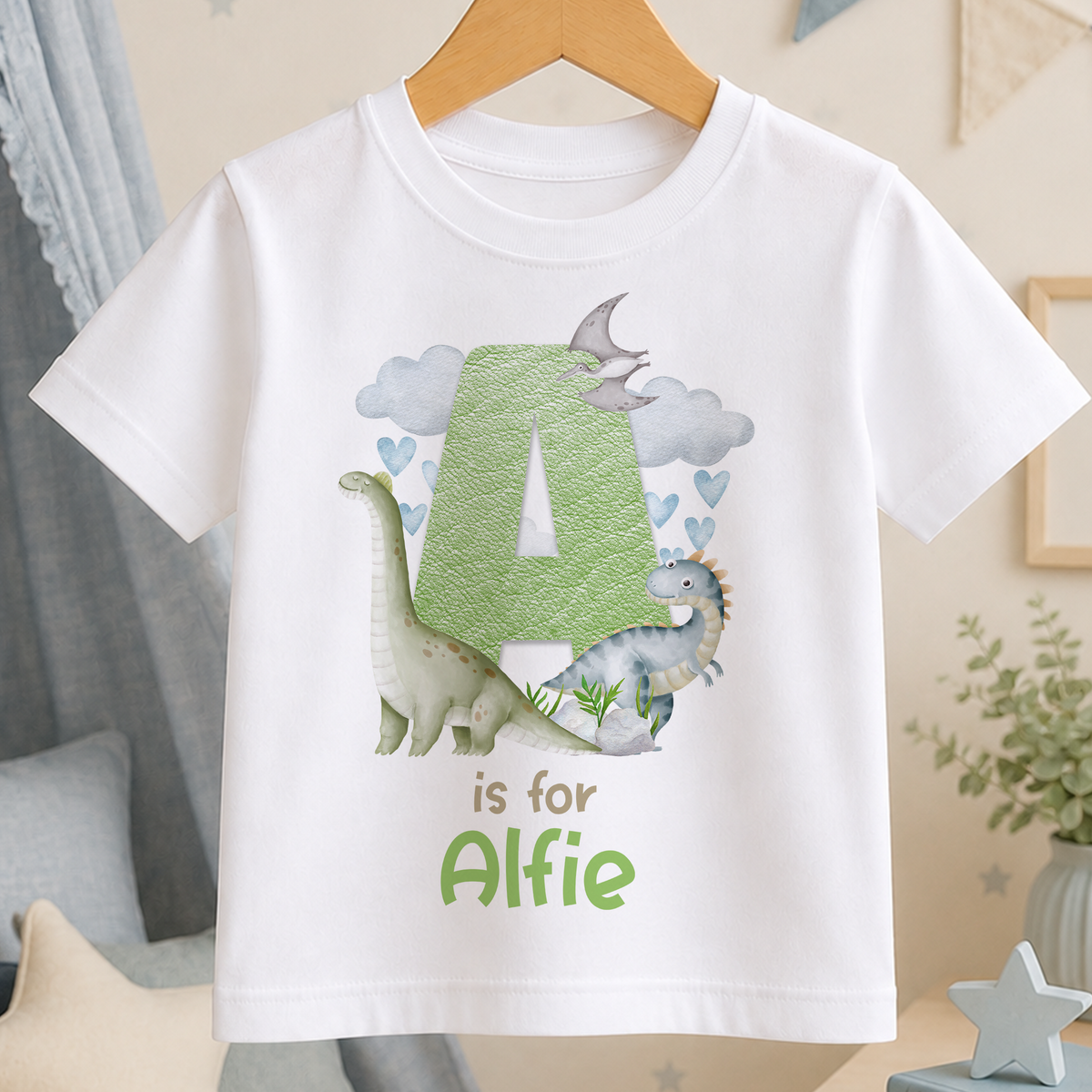 A white t-shirt with a green dinosaur graphic and the text "is for Alfie" printed on it.