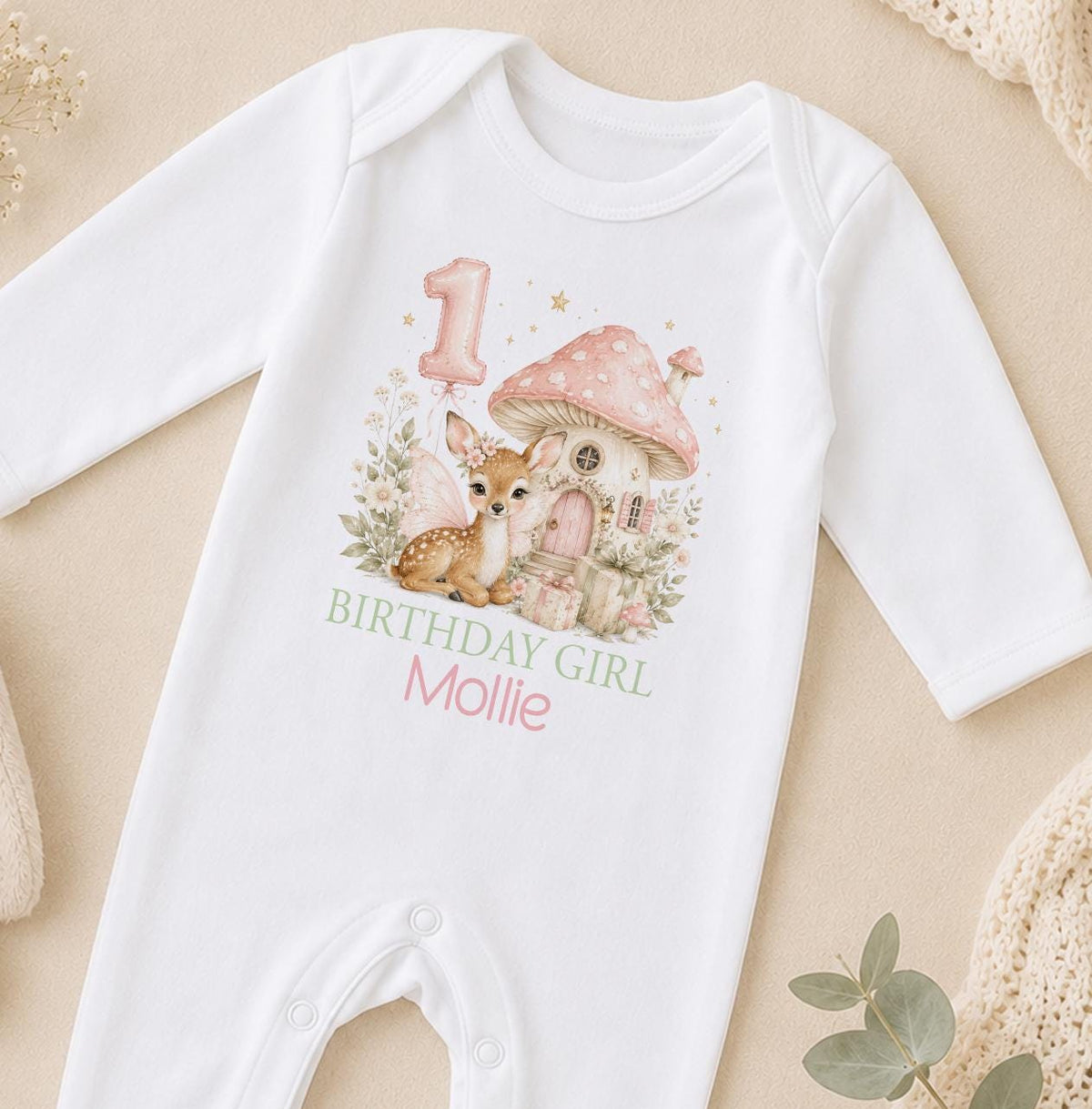 Personalised first birthday sleepsuit in white with a fairy fawn, pink toadstool house, number one balloon and Birthday Girl above a name
