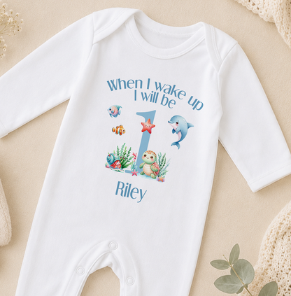 A white onesie with a personalized message and illustrations of marine animals, including a dolphin, starfish, and fish, printed on it.