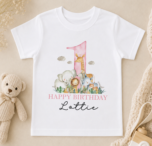 A white t-shirt with a pink number one and a cartoon illustration of various animals, including a giraffe, elephants, and a teddy bear, along with the text "Happy Birthday Lottie".