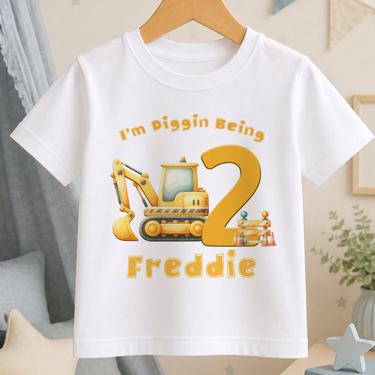 A white t-shirt with a yellow construction vehicle graphic and the text "I'm Diggin Being 2" printed on it.